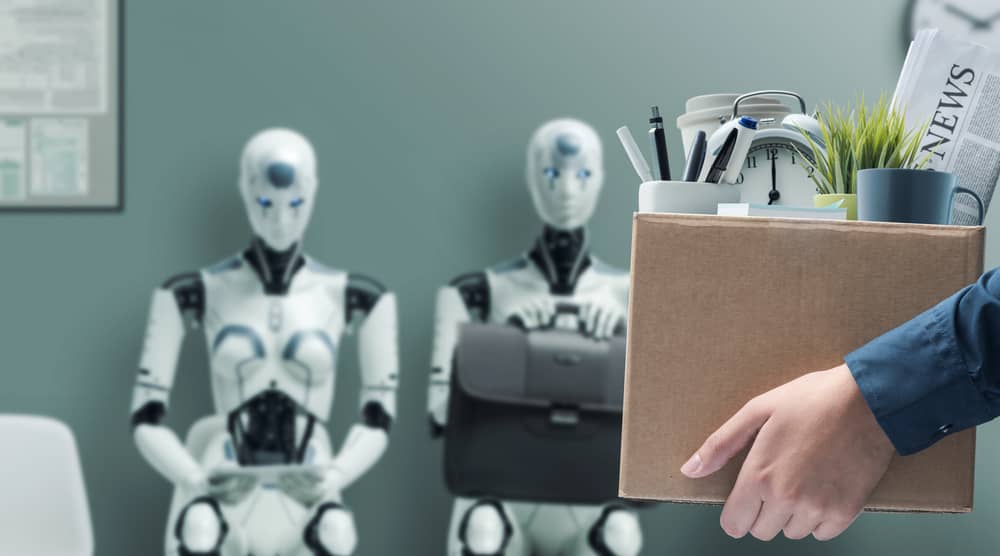 Descubre profesiones que desaparecen con la IA. Un empleado despedido lleva una caja, mientras dos robots humanoides esperan para reemplazarlo en su puesto de oficina.